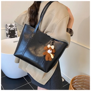 Detail view of black faux leather tote bag with brand logo and cute plush bear charm accessory