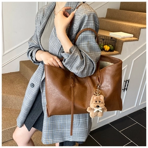 Close-up of a large dark brown faux leather tote bag with a cute plush bear charm