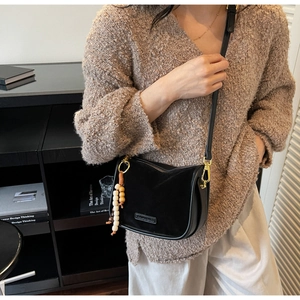 Detail of black crossbody bag featuring matte leather panels and bohemian wooden bead tassel