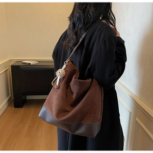 Detail of dark brown suede hobo bag with teddy bear charm shown in a minimalist room