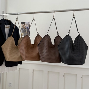Detail of woven texture bucket bags in beige, brown, and black hanging on a metal rod