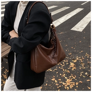 Vue détaillée du grand sac hobo marron foncé brillant avec accessoire rayé dans la rue