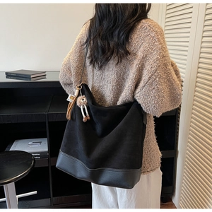 Detail of a large black suede tote bag with a cute bear charm on a model's shoulder