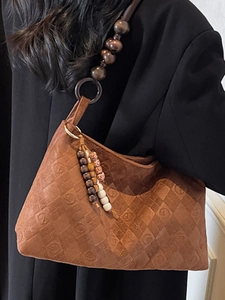 Brown suede underarm bag with embossed diamond patterns and wooden bead strap on model