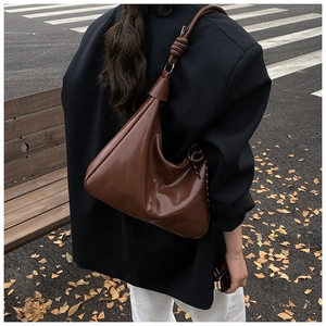 Détail du sac hobo en cuir verni marron avec bandoulière nouée dans une rue d'automne