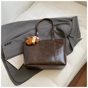 Detail of deep brown tote bag with bear charm on a grey suit jacket background