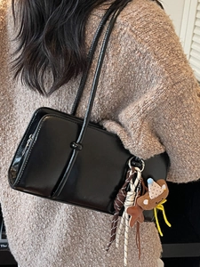 Sac baguette minimaliste en cuir noir avec breloque ours en peluche porté sur un pull beige