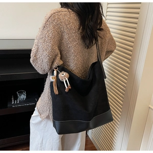 Macro detail of black hobo bag with plush doll charm and leather tassel accessory