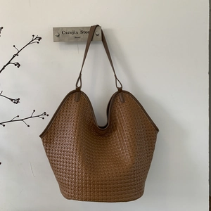 Detail of a brown woven leather tote bag hanging on a hook with elegant texture