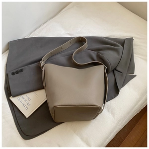 Close-up of taupe litchi grain leather bucket bag with silver hardware on a grey blazer
