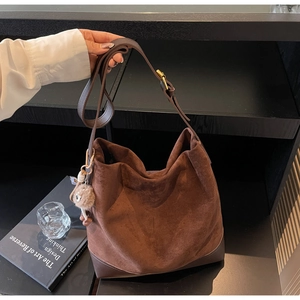 Detail of a large brown suede hobo bag with leather trim and soft fur ball charm