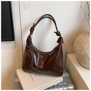 Détail du sac hobo en cuir poli marron foncé avec bandoulière nouée sur des livres
