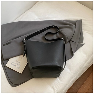 Detail of minimalist black bucket bag with lychee grain texture on gray blazer