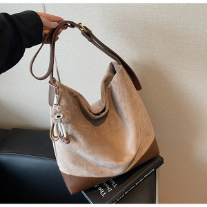 Detail view of large beige suede tote bag with brown leather trim and plush eye charm