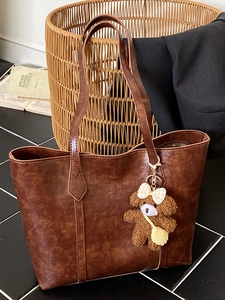 Dark brown retro tote bag in glossy leather with a cute plush bear charm for daily commute