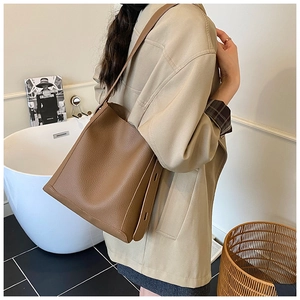 Detail of a large brown pebbled leather bucket bag with wide adjustable shoulder strap