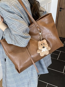 Brown large capacity tote bag with bear charm shown on model in a grey blazer jacket