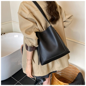 Detail view of black lychee grain leather bucket bag worn by a model in casual attire