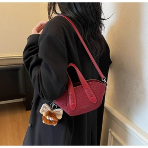 Dettaglio borsa a secchiello bordeaux in tessuto con ciondolo su cappotto nero