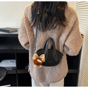 Dettaglio della borsa a secchiello nera minimalista con un ciondolo a mostro di peluche marrone