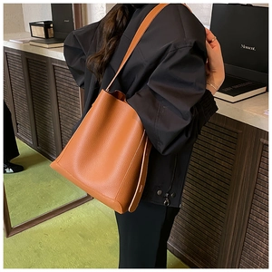 Detail of caramel leather bucket bag worn by model, showing premium pebbled texture