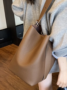 Minimalist brown pebbled leather bucket bag with adjustable wide strap shown on model