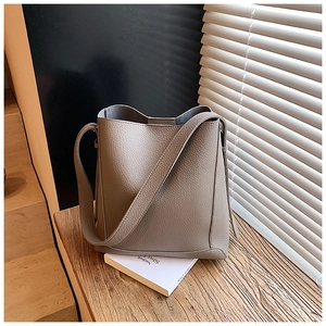 Close-up of taupe litchi grain leather bucket bag with wide strap on wooden desk