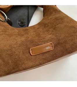 Gros plan sur la texture en daim marron du sac avec écusson logo et finitions soignées