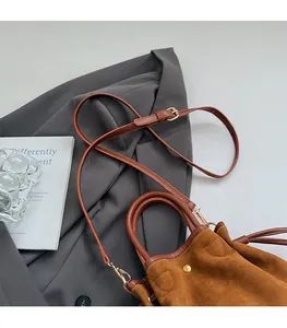 Detail of brown suede bucket bag with adjustable strap on a gray blazer background