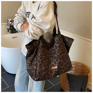 Detail of leopard print canvas tote bag with leather label on a shoulder strap model