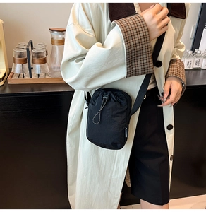 Detail of black drawstring crossbody bag with fashion label worn over a beige coat
