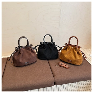 Close-up of drawstring bucket bags in suede finish showing handle and metal logo plate