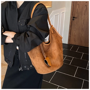 Brown suede tote bag detail with leather strap and decorative pendant on a model
