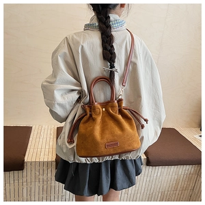 Detail view of caramel brown suede bucket bag with drawstring and leather logo tag