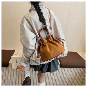 Detail of a brown suede drawstring bucket bag featuring a square fashion brand label