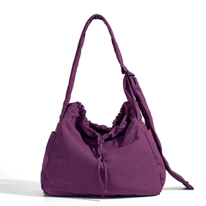 Detail view of purple drawstring nylon shoulder bag with adjustable strap and side pockets