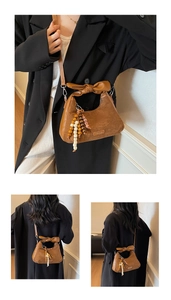 Détail du sac à bandoulière en daim marron avec poignée en cuir et pompons perlés
