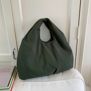 Dettaglio di una grande borsa hobo verde oliva in tessuto testurizzato su cuscino bianco