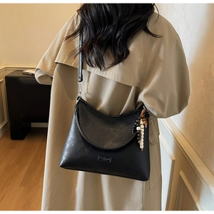 Detail of black pebbled leather crossbody bag with beaded charm on a beige coat