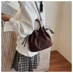 Detail of dark brown suede drawstring bucket bag with dual handles and leather shoulder strap