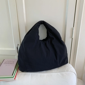 Borsa tote minimalista in tela nera su un divano bianco con luce naturale soffusa