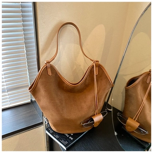 Close-up of brown suede bucket bag featuring a minimalist leather strap and glasses holder