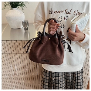 Detail of dark brown suede bucket bag featuring drawstring closure and textured leather
