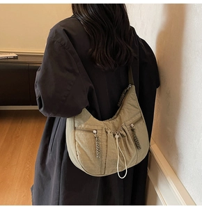 Detail of a green nylon crescent shoulder bag with functional multi-zipper pockets