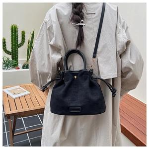 Detail of black suede bucket bag with drawstring and golden hardware on trench coat model