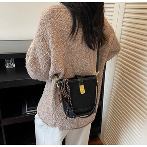 Λεπτομέρεια μαύρης καπιτονέ τσάντας με χρυσή κλειδαριά και λουράκι φορεμένη από μοντέλο