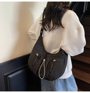 Detail view of large black crescent nylon shoulder bag on a model in a casual setting