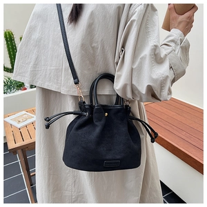 Detail view of black suede bucket bag with drawstring closure on a minimalist balcony