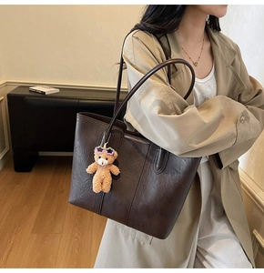 Detail of vintage coffee brown tote bag with bear charm on a beige trench coat