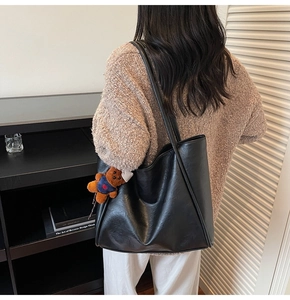Detail of a large black faux leather tote bag with a cute brown bear charm on shoulder